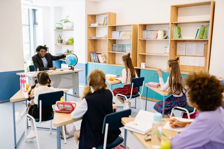 Ein Lehrer zeigt auf einen Globus auf seinem Schreibtisch, während eine vielfältige Gruppe von Schülern in einem Klassenzimmer zusieht