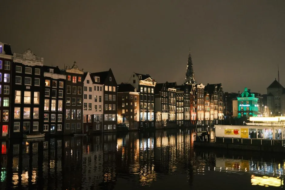 Fila de casas de canal de Ámsterdam con ventanas iluminadas reflejadas en el agua de noche