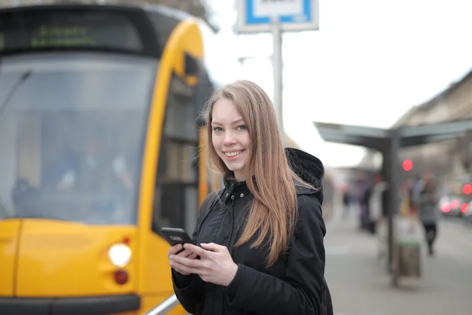 Una persona joven revisa su teléfono móvil mientras espera en una parada de tranvía