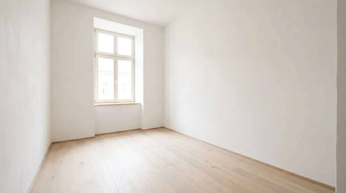 Ein helles, leeres Wohnungszimmer mit kahlen Wänden und einem Fenster, ohne Möbel oder Personen zu sehen