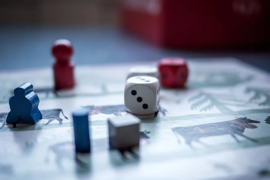 Primer plano de piezas de madera coloridas de un juego de mesa, dados y fichas esparcidas sobre un tablero ilustrado