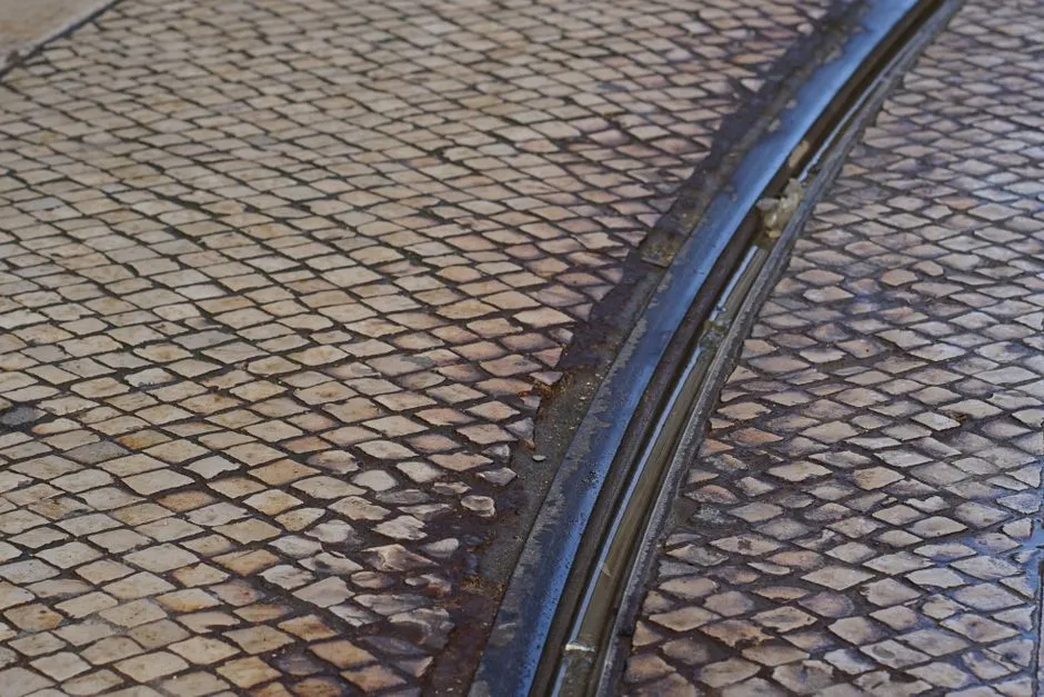 Primer plano de un raíl de tranvía curvándose por un pavimento de adoquines desgastado, sin personas visibles