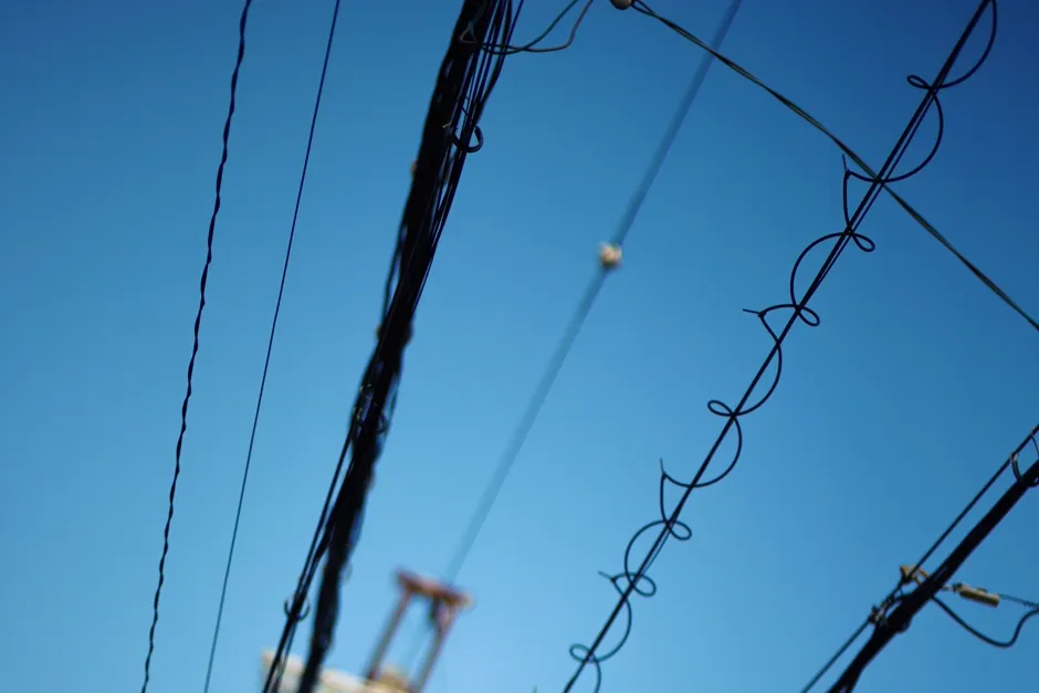 Vista de cerca de cables eléctricos aéreos cruzando contra un cielo azul despejado, un poste de servicios desenfocado al fondo, sin personas, texto, ni logotipos visibles
