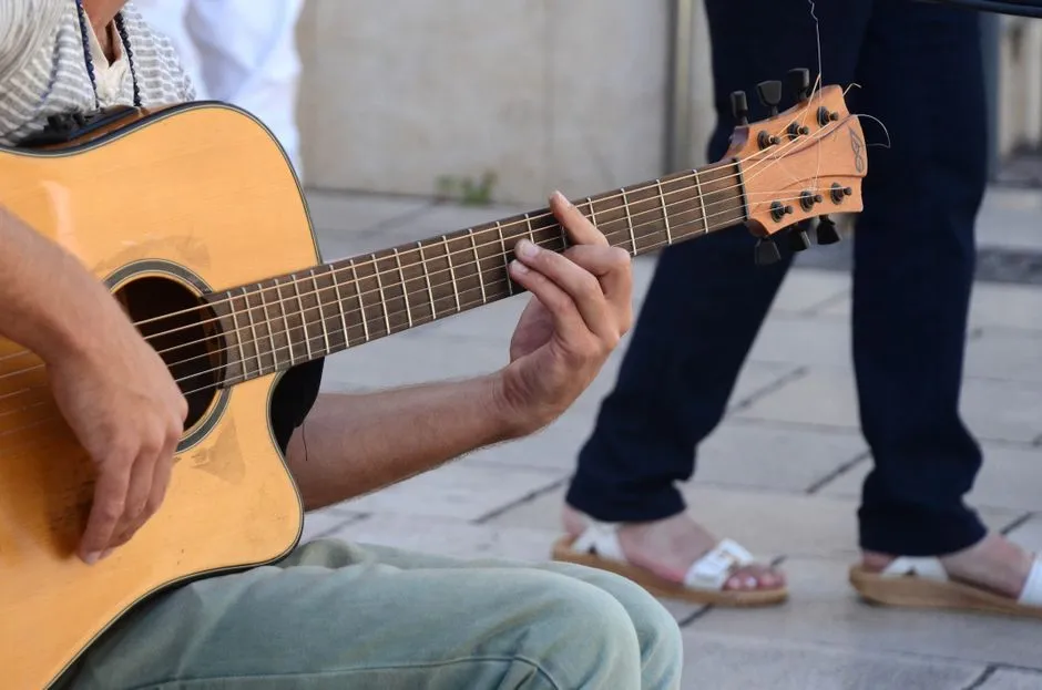 Primer plano de manos tocando una guitarra acústica al aire libre en una calle de la ciudad
