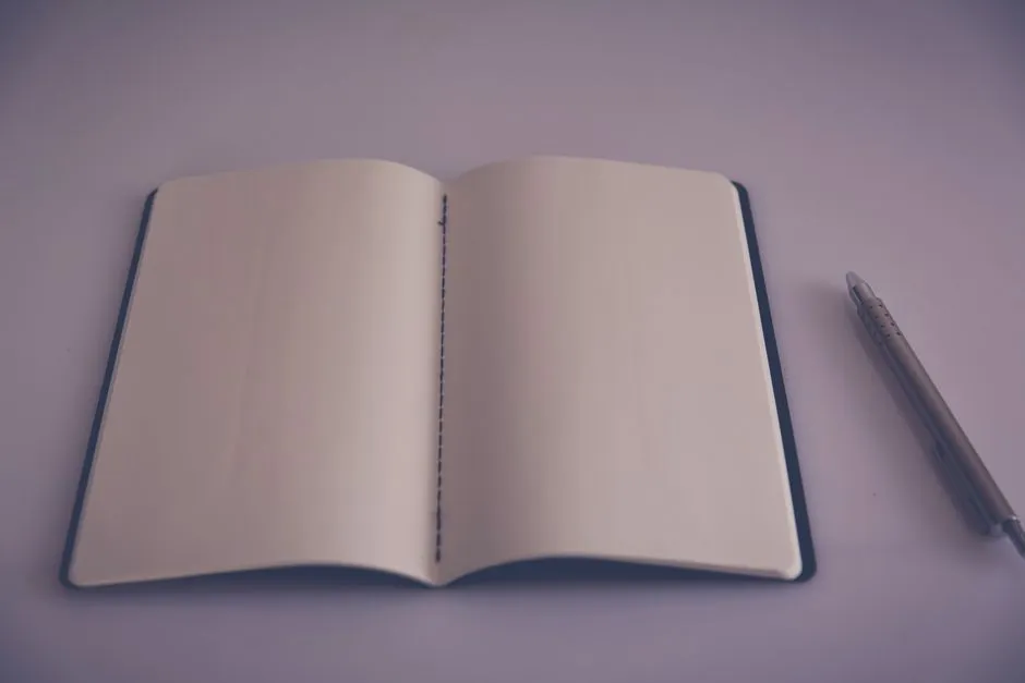 Ein aufgeschlagenes leeres Notizbuch und ein Stift auf einem schlichten Schreibtisch, bereit für den Papierkram