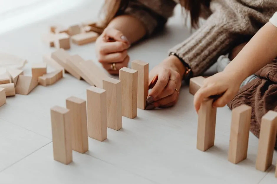 Close-up of an adult's and a child's hands lining up small wooden blocks together on a light wooden floor