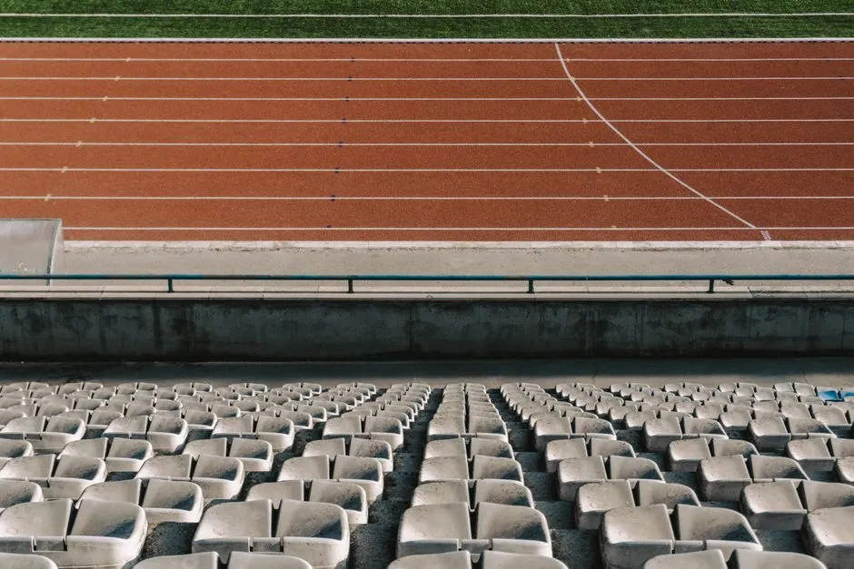 Leere rote Laufbahnen einer Leichtathletikanlage, dahinter Reihen leerer Betonsitze eines Stadions, keine Personen sichtbar