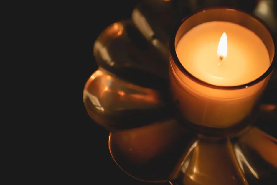 A single lit candle glowing in a glass holder against a dark background, no people visible