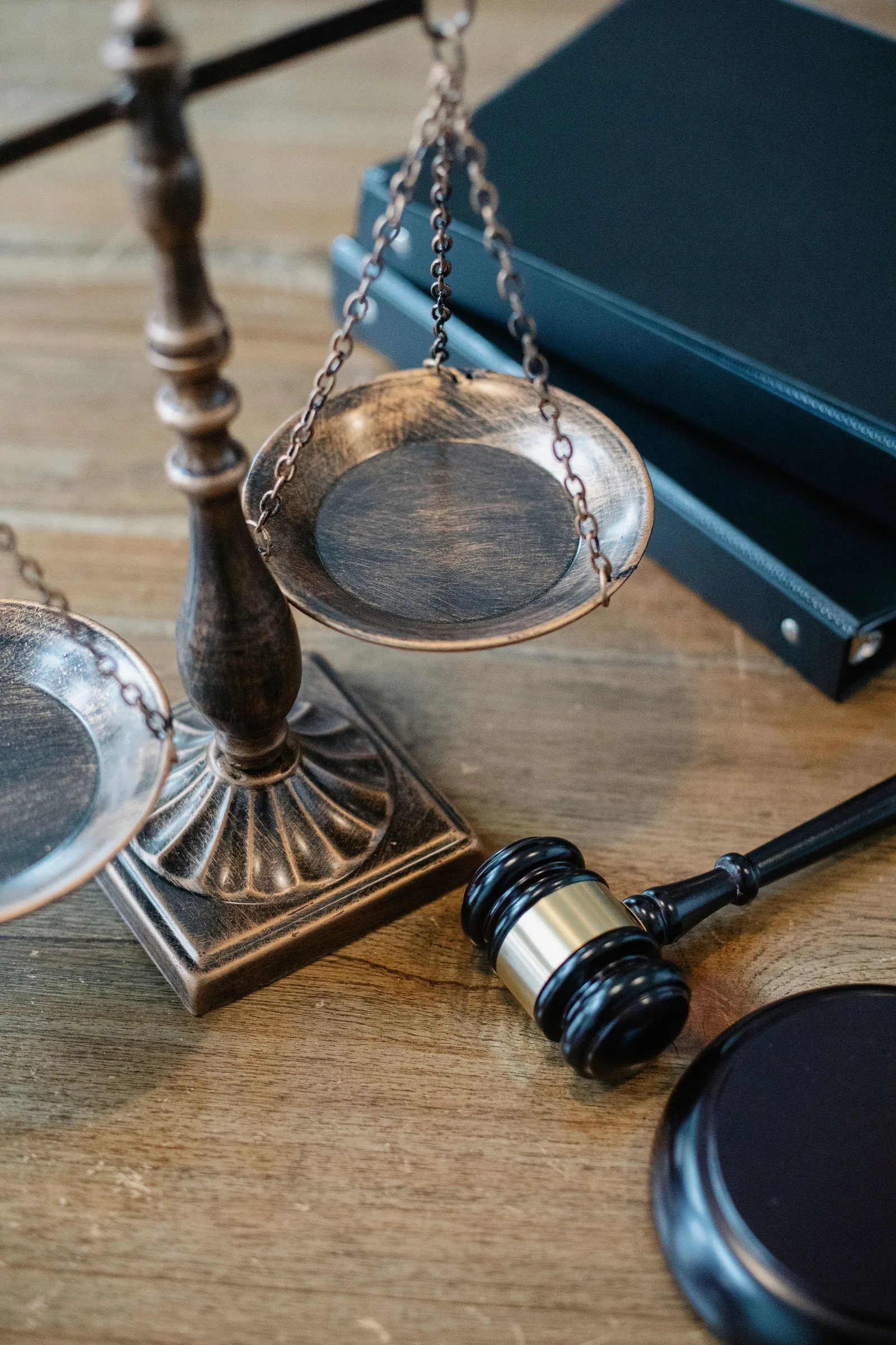 Una balanza de la justicia de bronce y un pequeño mazo de juez sobre un escritorio de madera junto a una carpeta oscura, sin texto ni personas visibles