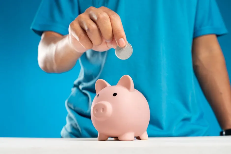 Eine Hand wirft eine einzelne Münze in ein kleines rosa Sparschwein