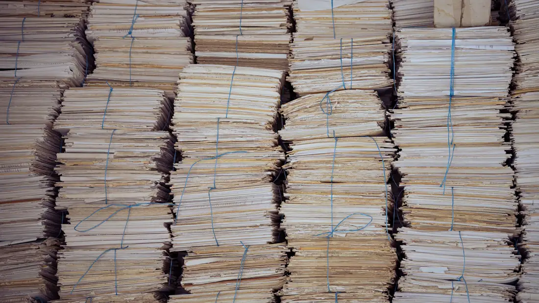 Altas pilas de documentos de papel envejecido atados con cordel azul, dispuestas en filas apretadas