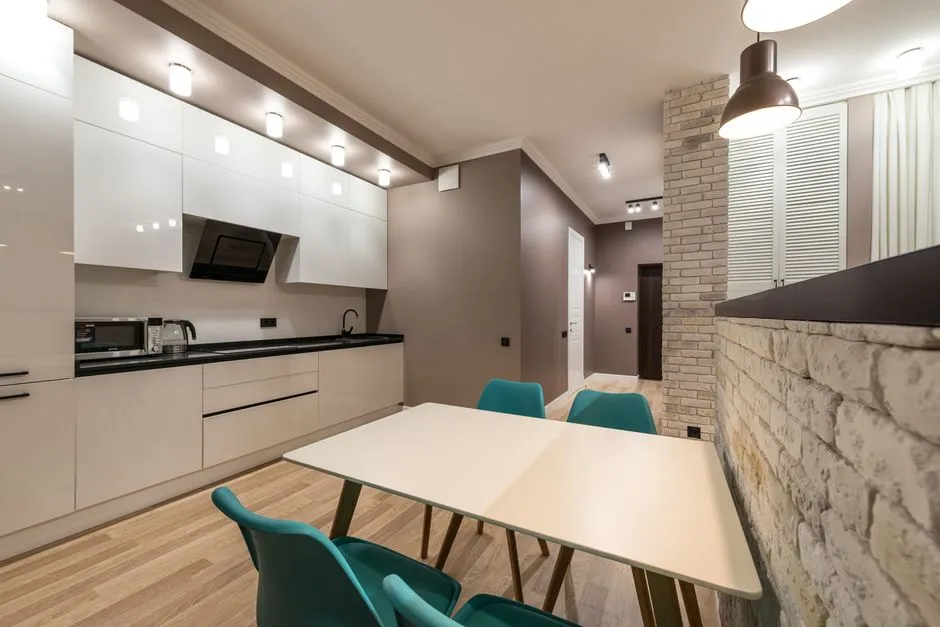 Beyaz dolapları, bir yemek masası ve sarkıt aydınlatması olan aydınlık bir dairede modern, donatılmış bir mutfak