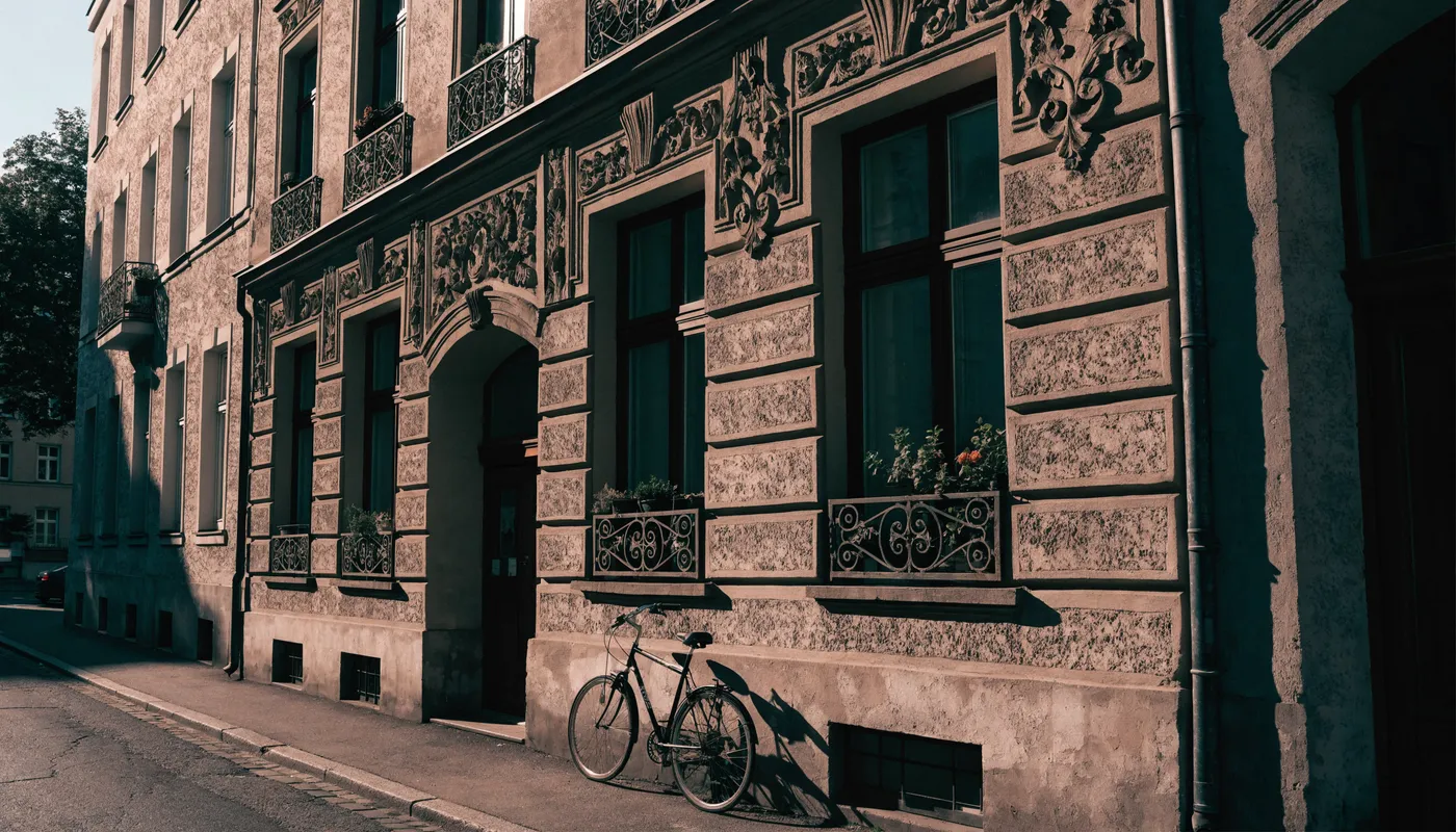 Fachada de un edificio de apartamentos Altbau de Berlín con marcos de ventana de estuco ornamentado y balcones de hierro forjado, una bicicleta apoyada en la pared cerca de la entrada