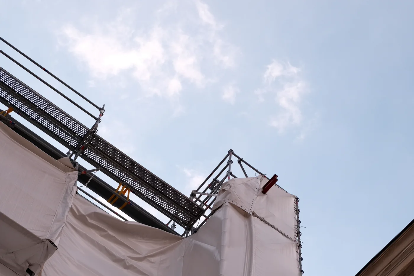 Barandillas de andamio y una lona protectora envolviendo la esquina de un edificio en renovación, visto desde abajo contra un cielo azul