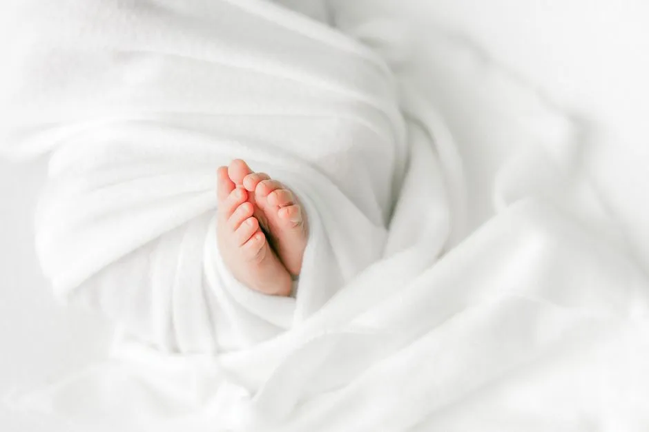 Los pies descalzos de un recién nacido asomando de una manta suave y blanca para envolver