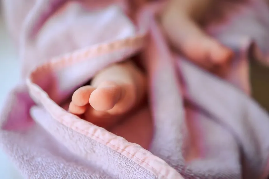 Nahaufnahme der nackten Füßchen eines Neugeborenen, eingewickelt in eine weiche rosa Decke