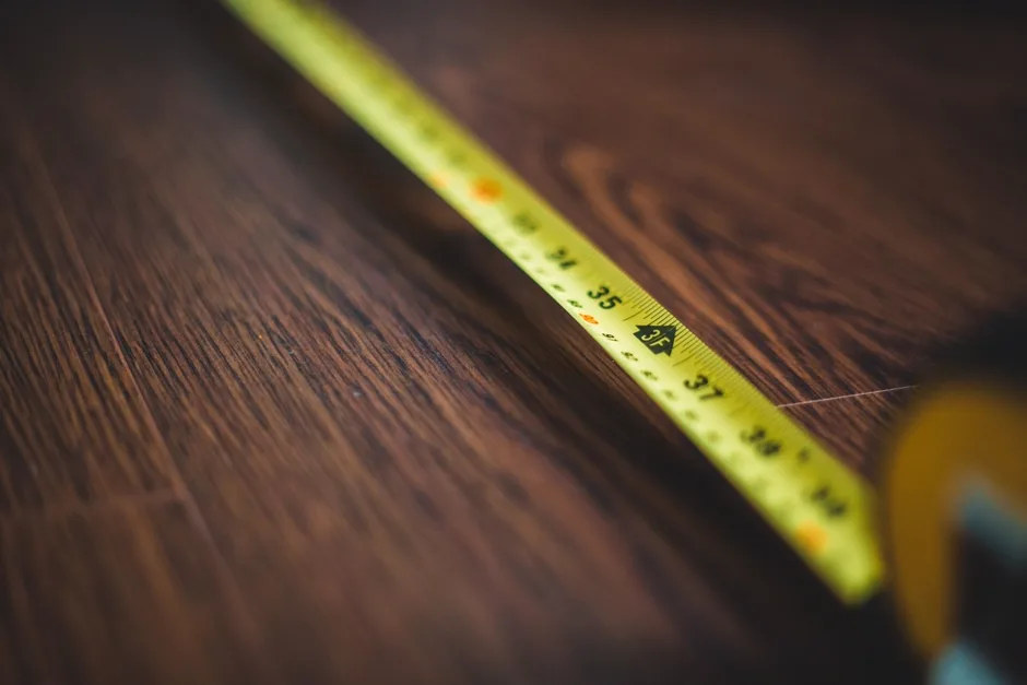 Close-up of a yellow measuring tape extended across a dark wooden floor, showing centimeter markings