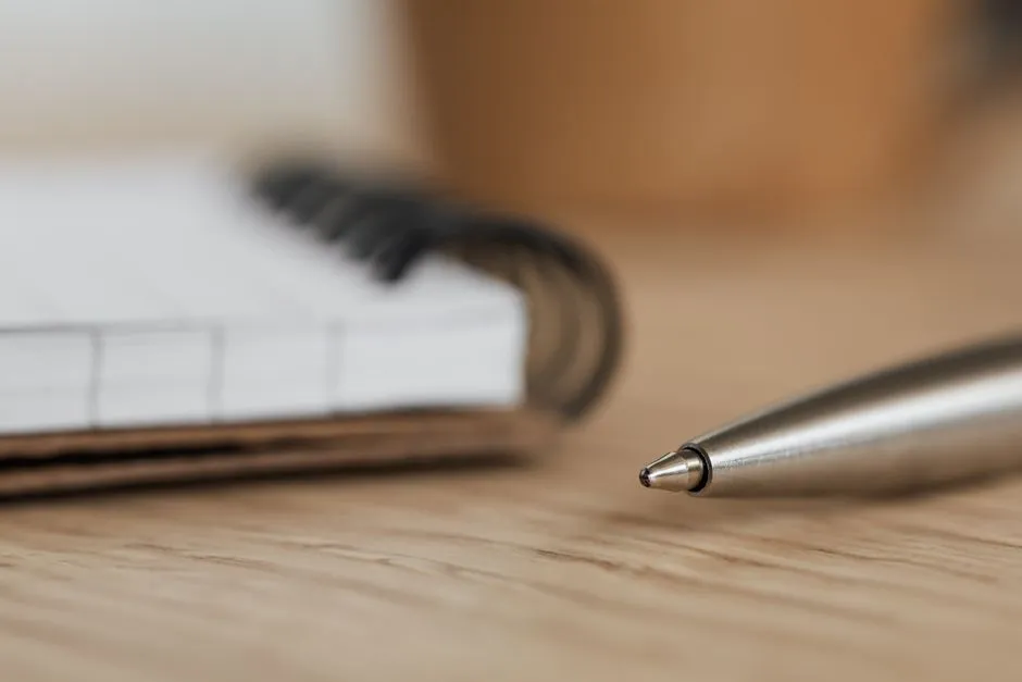 Nahaufnahme eines geöffneten Spiralnotizbuchs mit leeren linierten Seiten neben einem silbernen Stift auf einem Holzschreibtisch, sanft unscharfer Hintergrund, keine Personen sichtbar