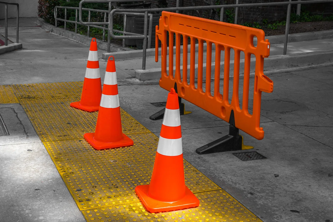 Conos de tráfico naranjas y una puerta de barrera de plástico bloqueando un paseo pavimentado, sin vehículos, señales ni personas visibles