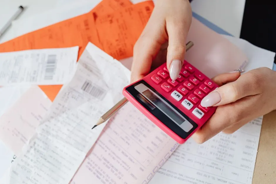 Un primer plano de manos sumando una pila de recibos de papel con una calculadora roja y un lápiz, el tipo de contabilidad detallada y numerada que exigen las propias reglas de Berlín para el dinero de la Klassenfahrt
