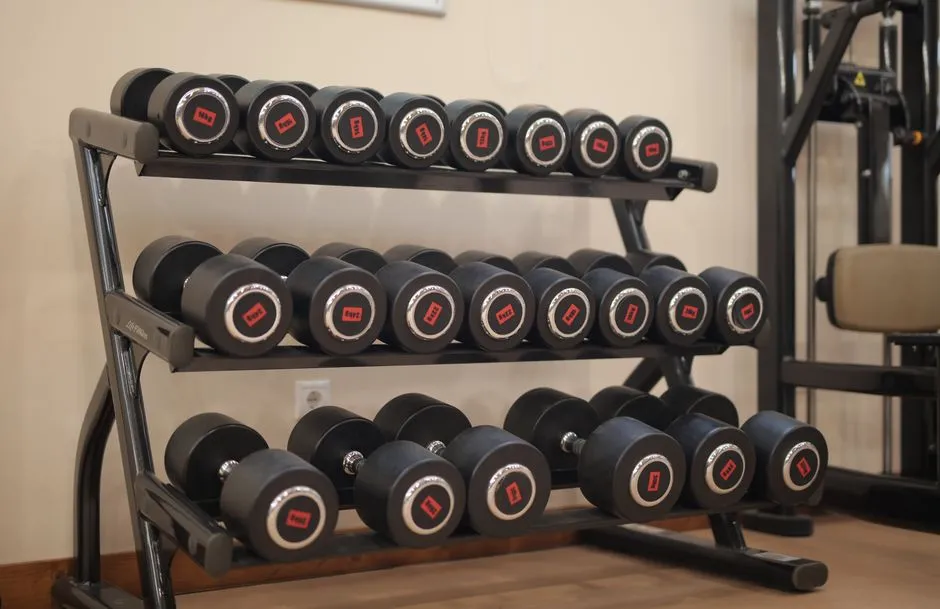 Estante de mancuernas negras con pequeñas etiquetas de peso rojas alineadas en filas sobre el suelo de un gimnasio