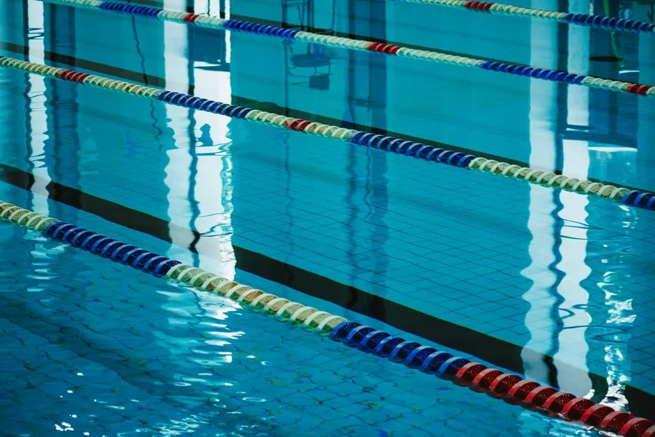 Piscina exterior vacía con largas cuerdas de carril extendiéndose hacia el extremo lejano, agua azul con suave oleaje, sin nadadores presentes