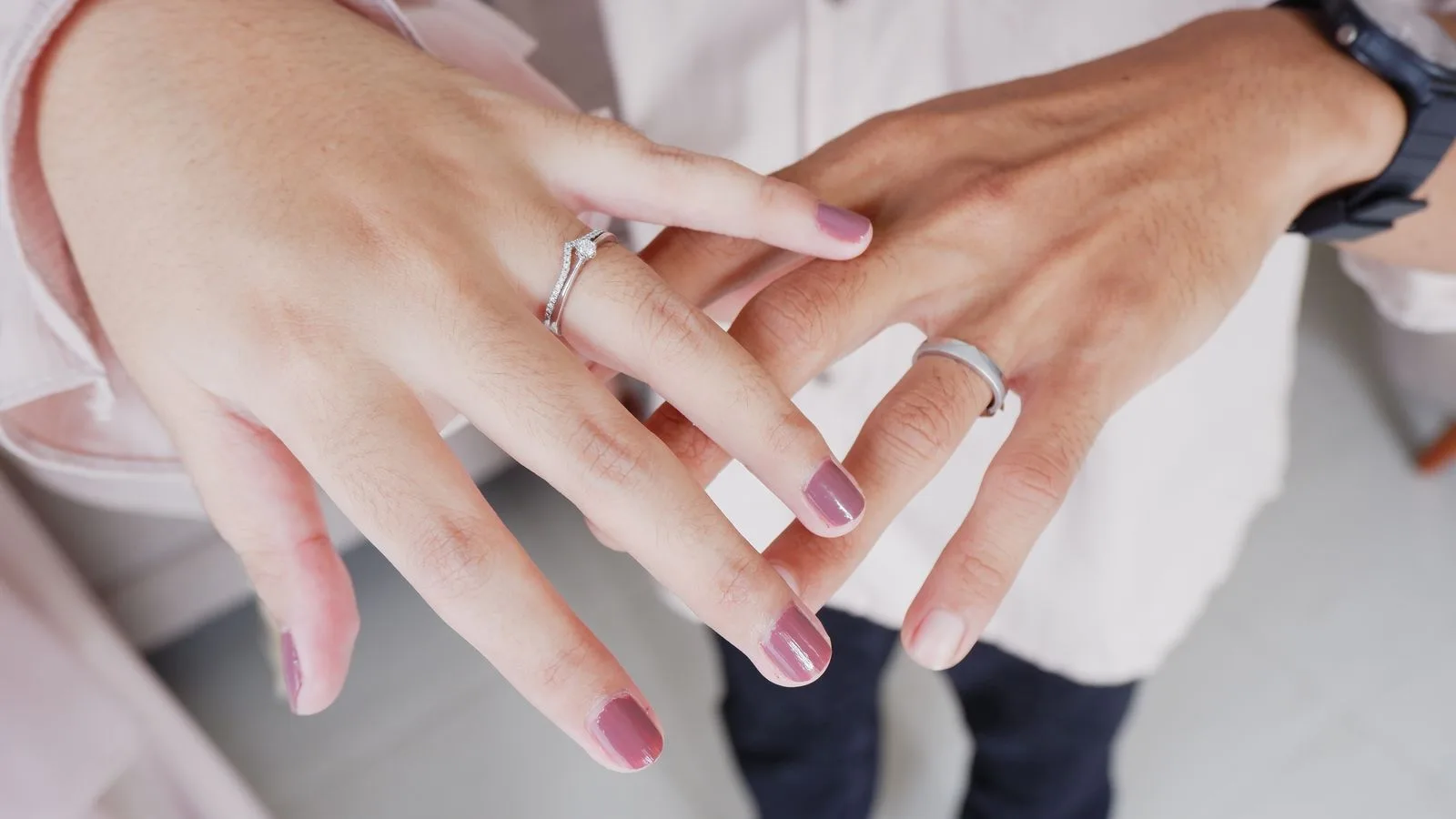 Primer plano de las manos entrelazadas de una pareja mostrando un anillo de boda y un anillo de compromiso, sin rostros ni texto visible