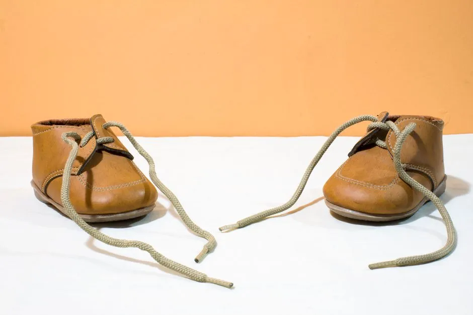 Un solo par de pequeños zapatos de niño pequeño de cuero marrón con cordones desatados descansando sobre una superficie clara