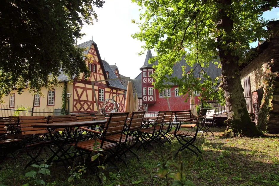 Traditionelles Fachwerkwirtshaus mit Außenhof, Holztischen und -stühlen unter belaubten Bäumen