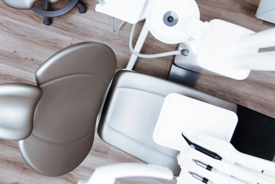 Yukarıdan görünen boş bir diş tedavi koltuğu, etrafında düzenlenmiş alet tepsileri ve ekipmanla