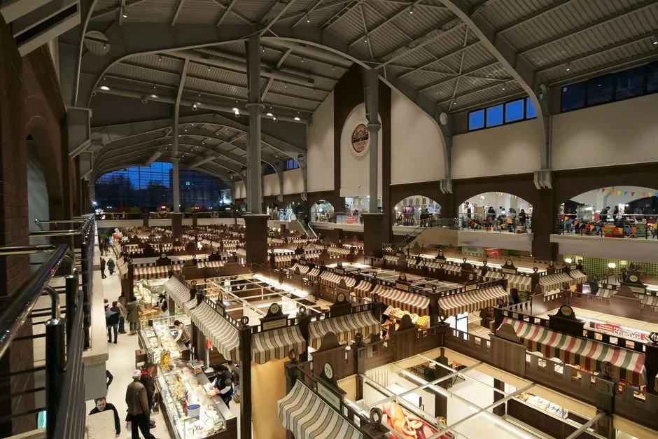 Innenansicht einer überdachten Markthalle mit Reihen gestreifter Markisen über einzelnen Verkaufsständen