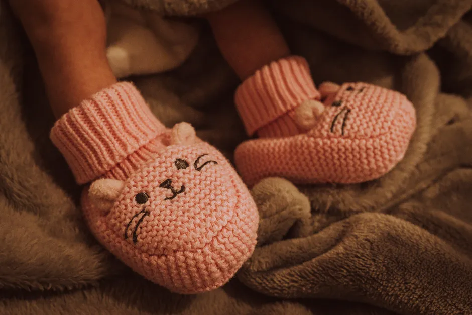 Yumuşak bir battaniyeye sarılmış, pembe örgü patik giymiş bir yenidoğanın çıplak ayakları