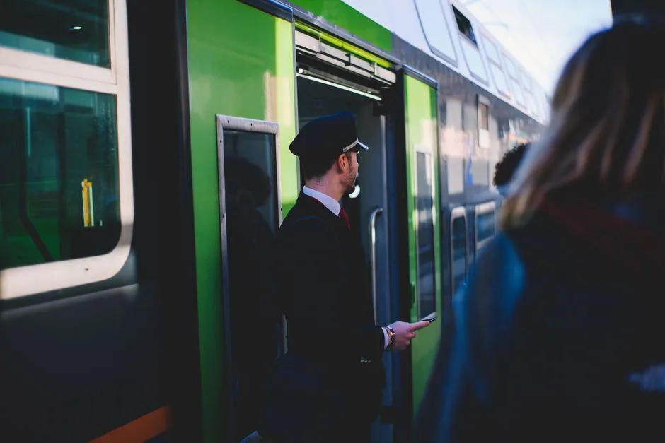Ein uniformierter Zugbegleiter steht an einer offenen Zugtür und hält ein Ticket, während er Fahrgäste kontrolliert