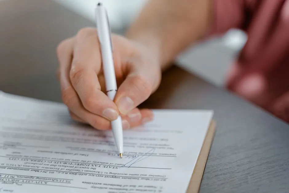 A close-up of a hand signing a printed document with a pen at a desk