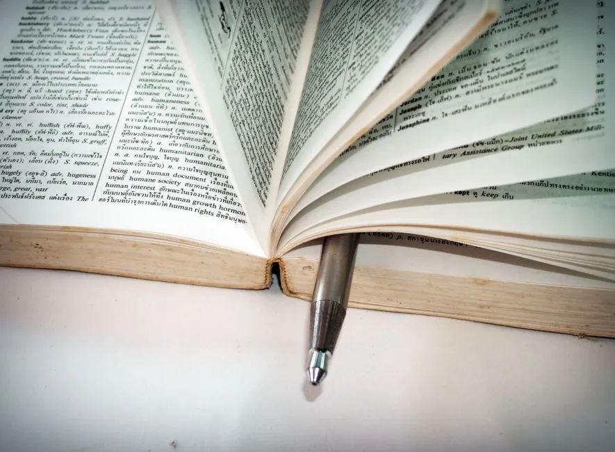 قاموس ثنائي اللغة مفتوح وقلم مستريح بين الصفحات