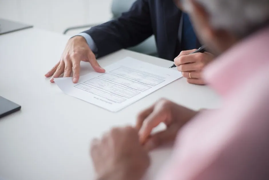 Un primer plano de manos revisando y firmando papeleo sobre un escritorio de consulta
