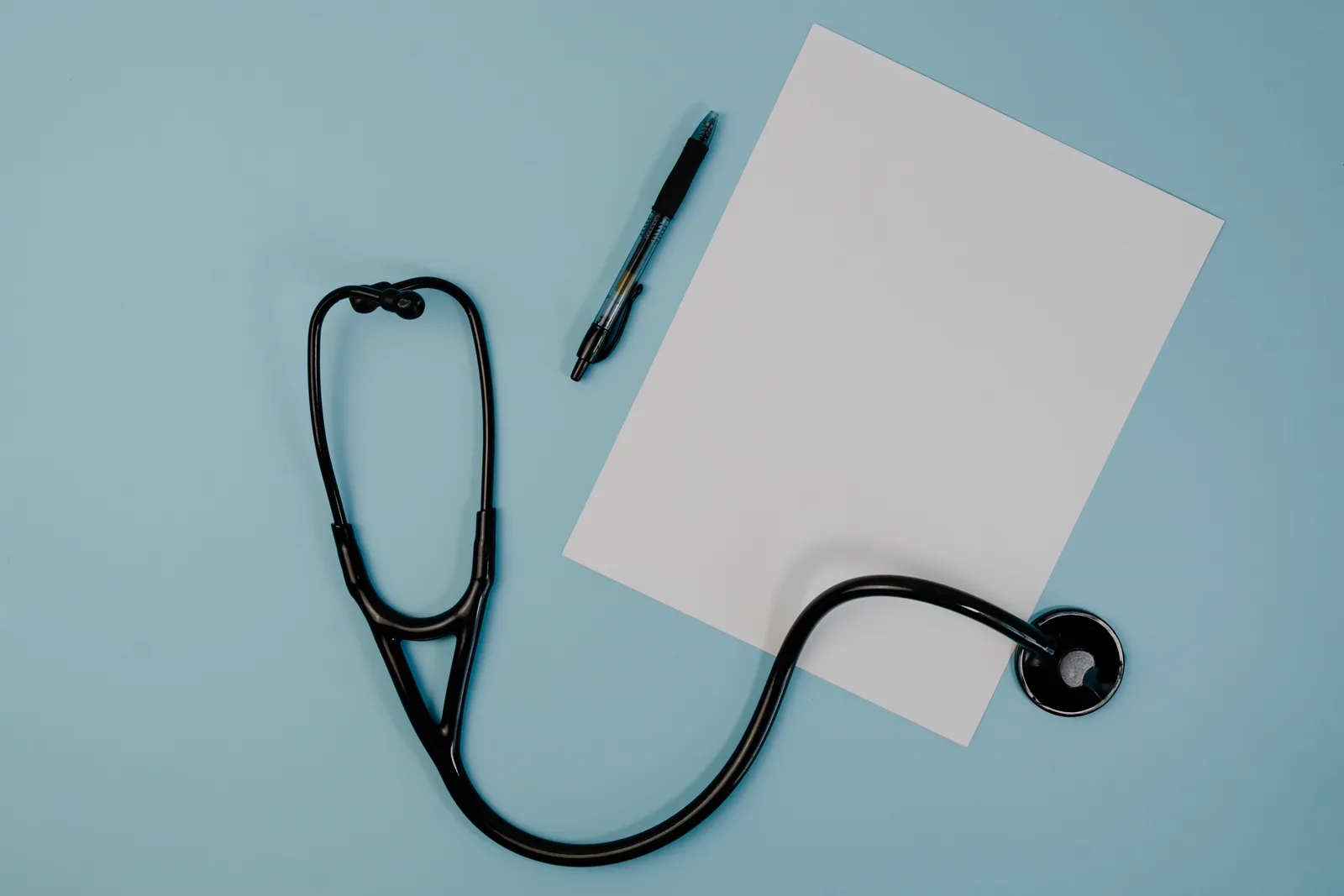 Ein schwarzes Stethoskop, ein Stift und ein leeres Blatt Papier auf einem Schreibtisch, sinnbildlich für einen laufenden Anerkennungsantrag im medizinischen Bereich