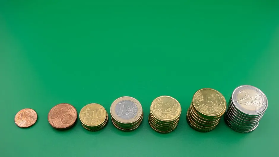 Reihen von Euromünzen in aufsteigenden Stapeln, von einem Cent bis zwei Euro, auf einer schlichten grünen Fläche