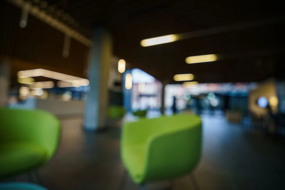 A blurred, softly lit modern office lobby with green lounge chairs, no readable text or identifiable people visible