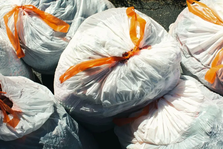 Varias bolsas de basura blancas atadas con lazos de plástico naranja, apiladas juntas al aire libre, sin personas ni texto legible visible