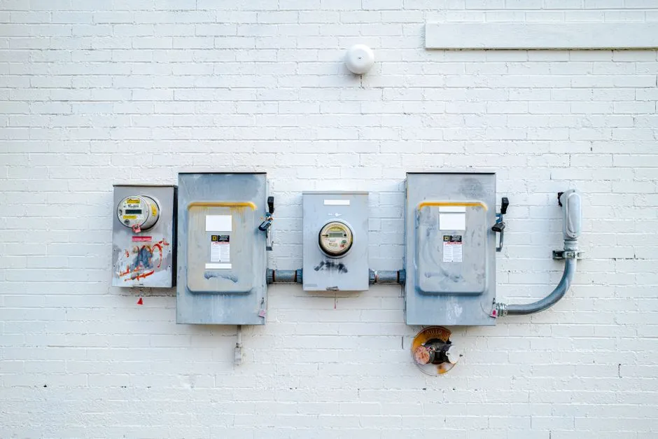 A row of grey electrical meter and breaker boxes mounted on a light brick exterior wall, no readable text or people visible