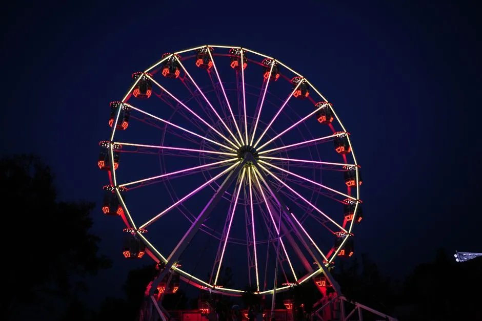 A brightly lit Ferris wheel glowing red and purple against a dark night sky at a funfair, no people or readable signage visible