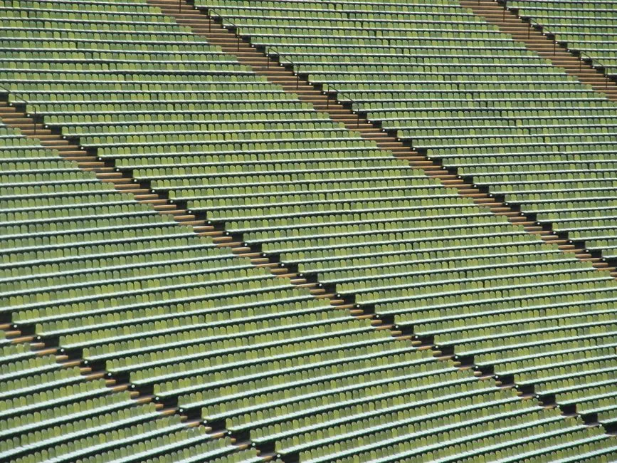Rows of empty stadium terrace seating seen from above, in muted green tones, with no people, logos, or readable signage visible