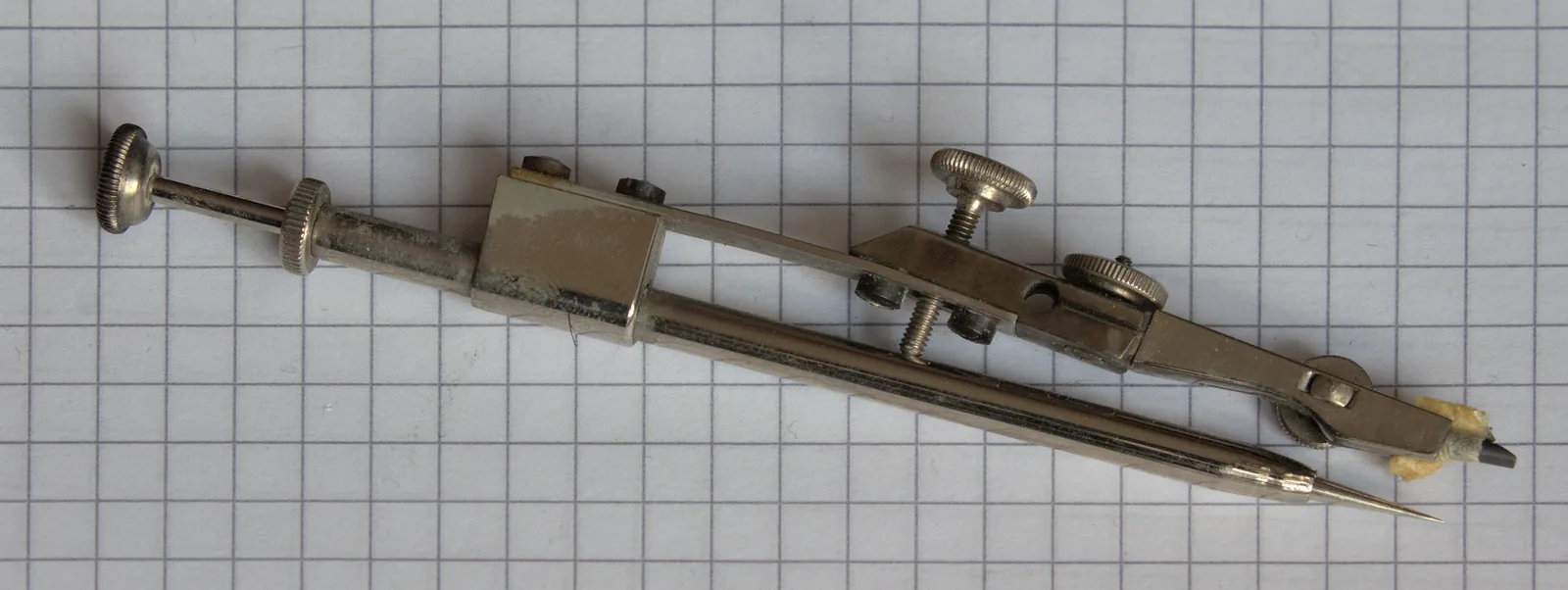 A vintage adjustable drafting compass with a pencil tip, resting on graph paper