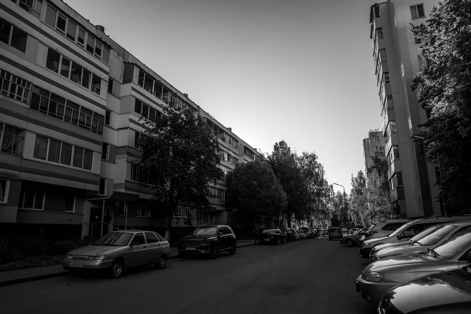 Schwarz-weiße Ansicht einer Wohnstraße mit geparkten Autos zwischen Wohnhäusern