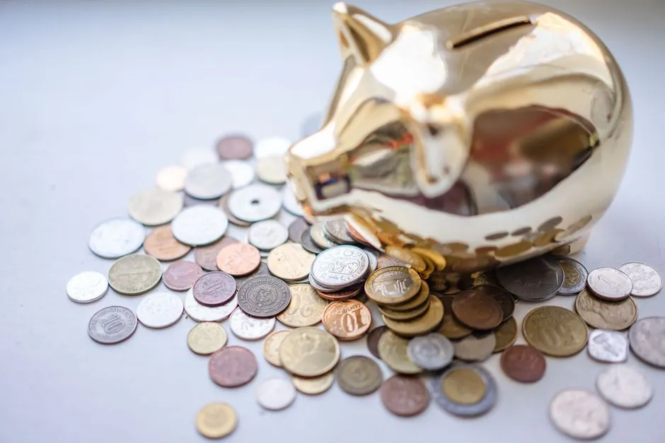 Ein goldenes Sparschwein umgeben von einem verstreuten Haufen verschiedener Eurocent- und kleiner ausländischer Münzen auf einer schlichten hellen Oberfläche