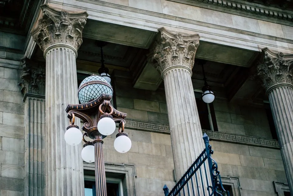 Columnas clásicas ornamentadas y una farola decorativa en el exterior de un edificio gubernamental de piedra, visto desde abajo