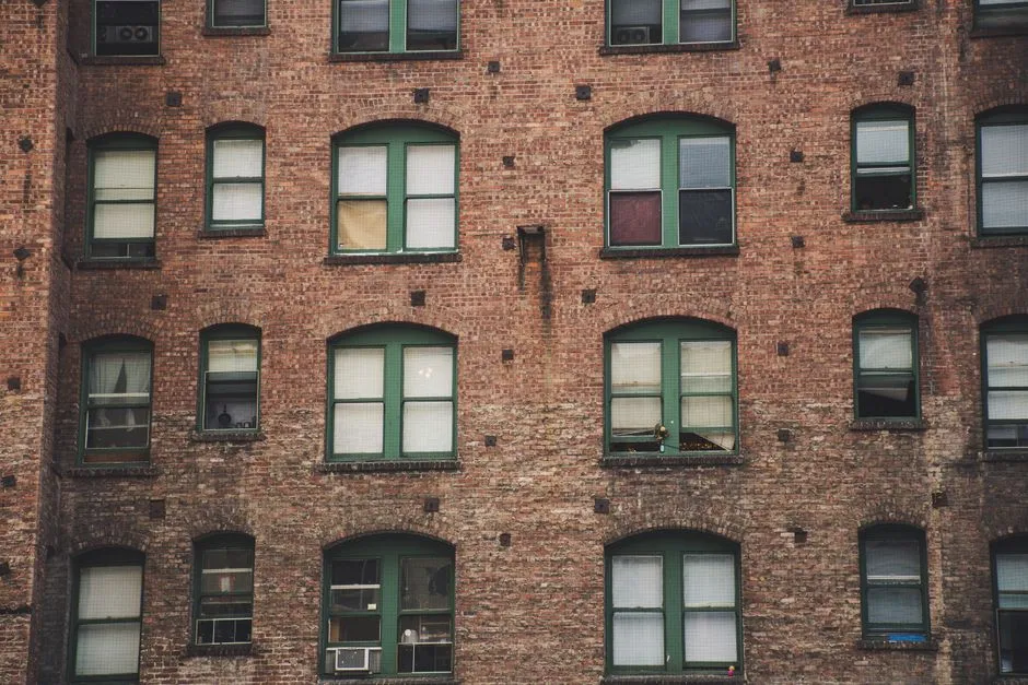 Eine Backsteinfassade eines Wohnhauses mit Reihen von Bogenfenstern, grünen Fensterrahmen und zugezogenen Vorhängen, ruhig und still, keine Menschen sichtbar