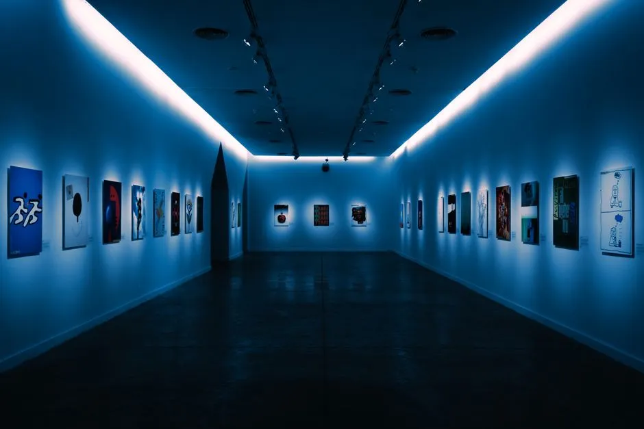 Yumuşak mavi tavan aydınlatması altında küçük çerçeveli sanat eserlerinin sıralandığı loş bir müze galeri koridoru, insan görünmüyor