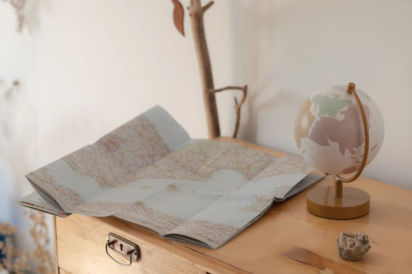 Un globo terráqueo de tonos pastel junto a un atlas de carreteras abierto sobre una cómoda de madera